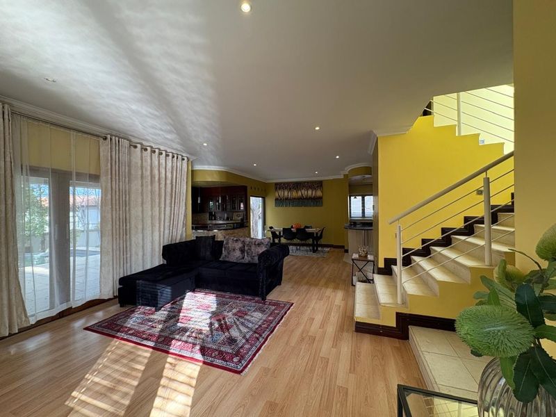 Spacious open-plan living and dining area featuring laminate flooring, a prominent staircase, and direct access to the outdoor patio through sliding glass doors.