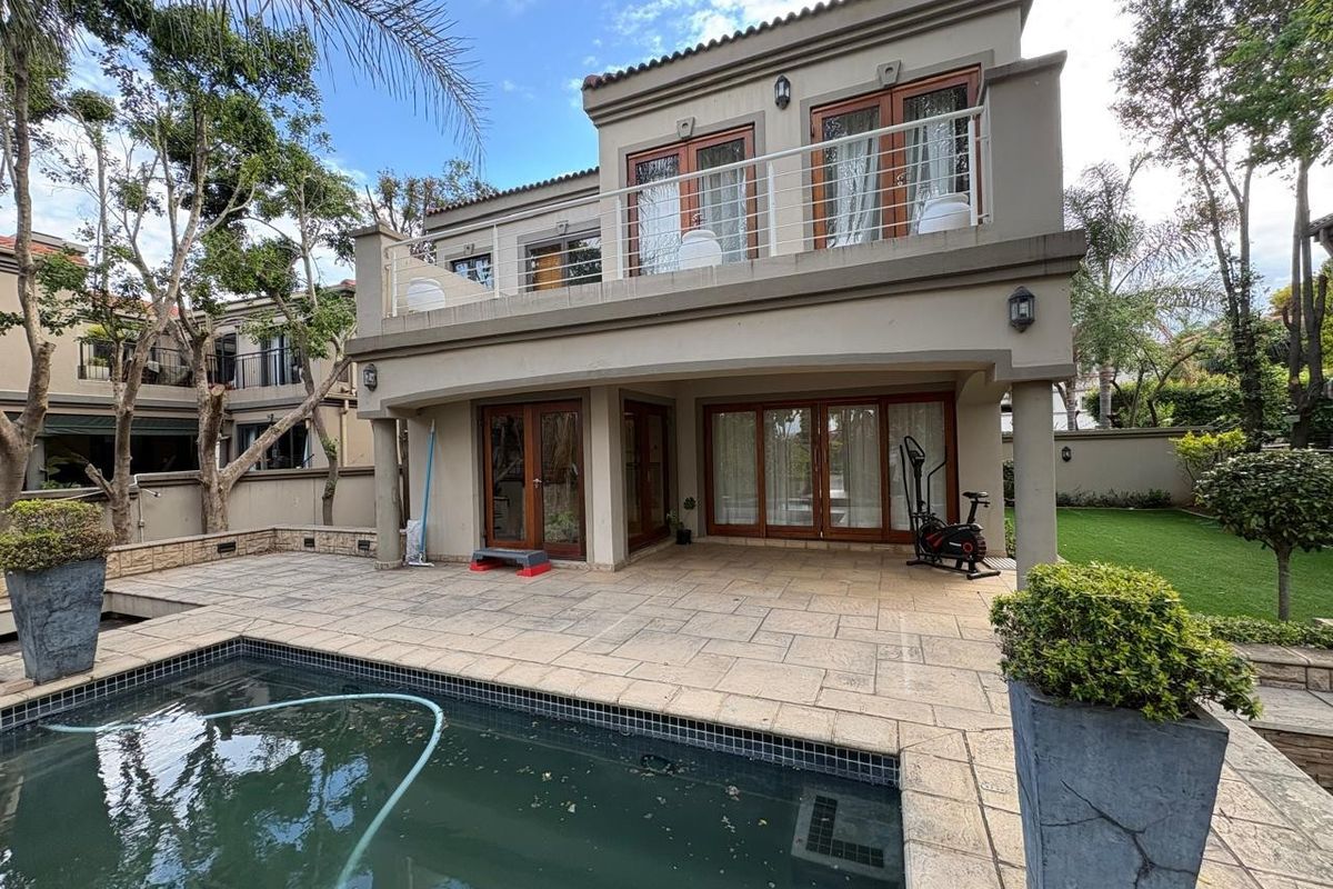 Rear view of a two-story house featuring a paved patio, swimming pool, and an upper-level balcony with glass doors.