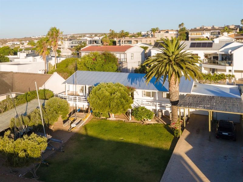 Aerial view of a residential property featuring a metal roof, spacious lawn, timber deck, and a covered carport area.
