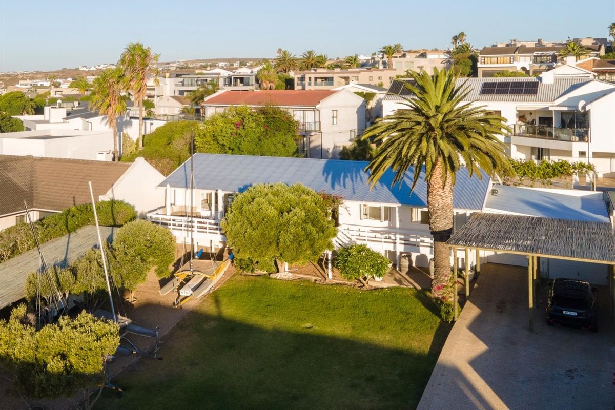 Aerial view of a residential property featuring a metal roof, spacious lawn, timber deck, and a covered carport area.