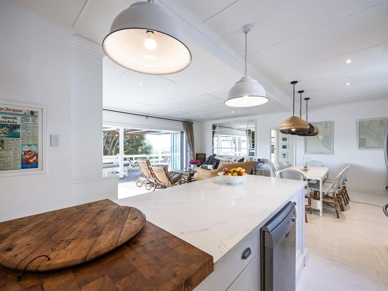Bright open-plan kitchen and living area featuring a stone-topped island, modern pendant lighting, and seamless flow to an outdoor patio through bi-fold doors.