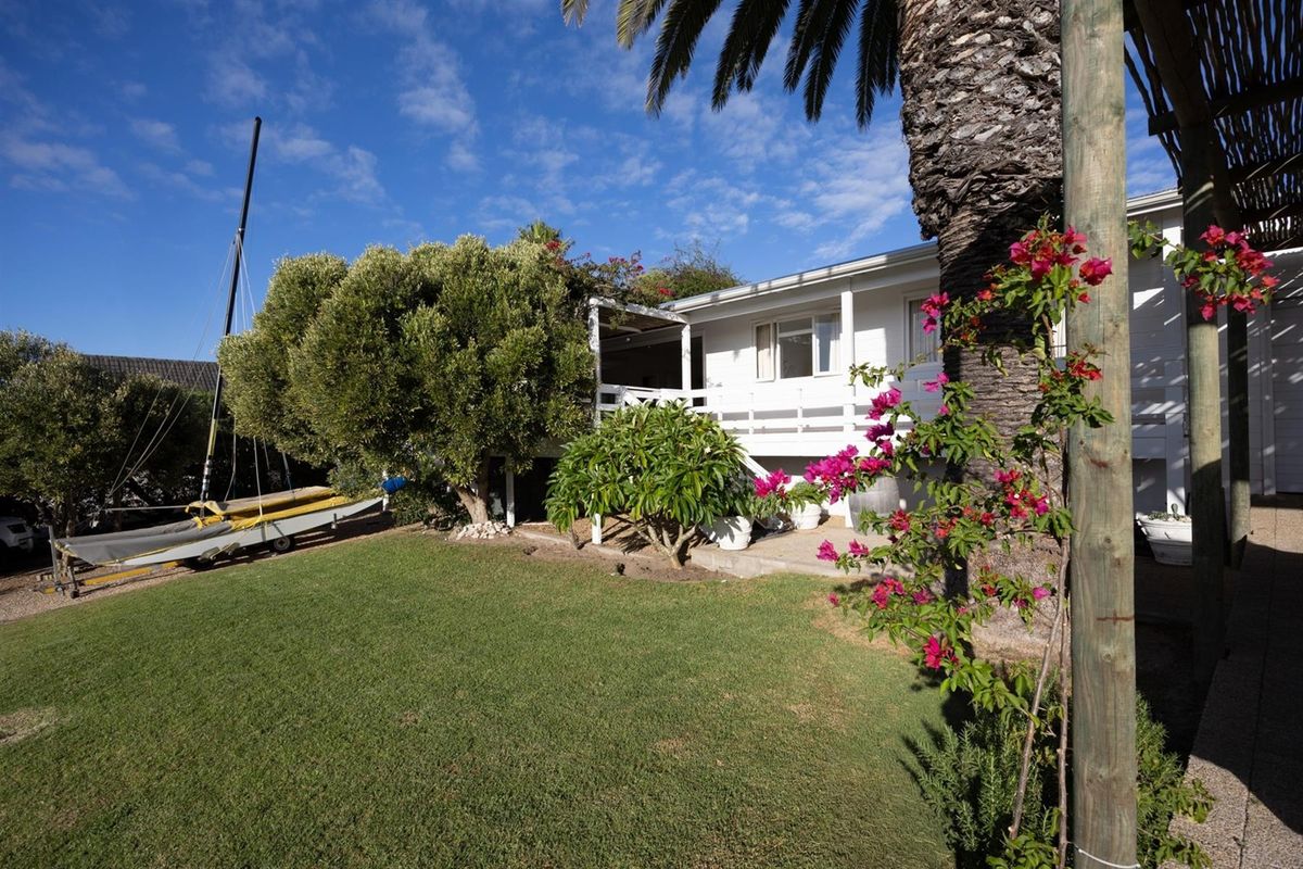A rear view of the property featuring a raised wooden deck, established garden, and mature trees under a clear blue sky.