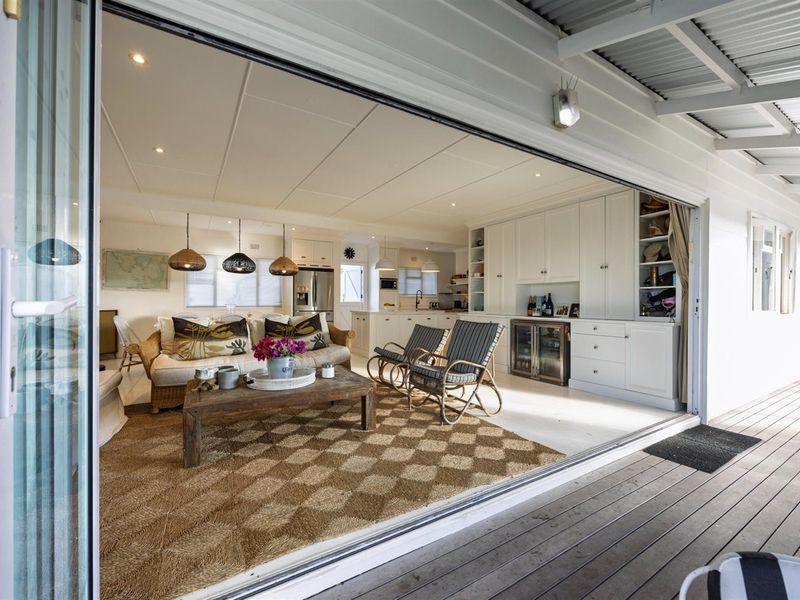 Spacious open-plan living area featuring built-in cabinetry, integrated wine storage, and seamless flow to a covered timber deck through large sliding glass doors.