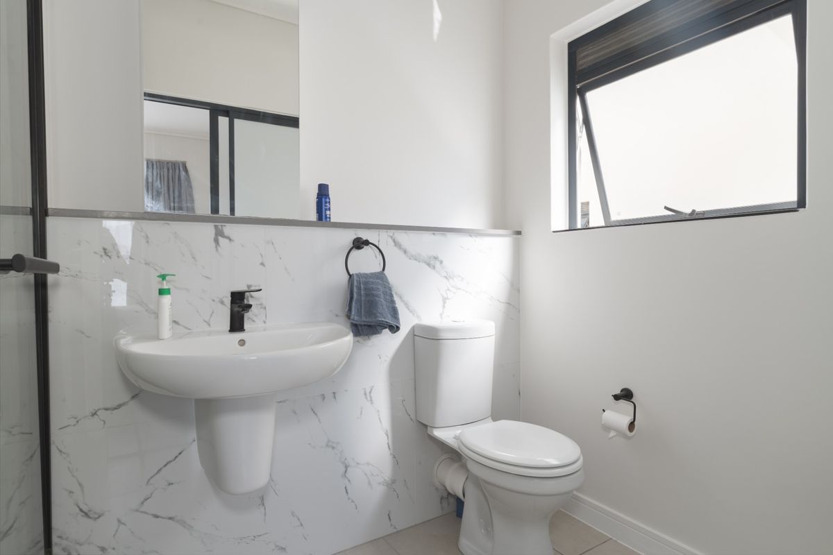 Modern bathroom featuring a pedestal washbasin, toilet, and elegant marble-look wall tiles with contemporary black fixtures and a functional top-hung window.