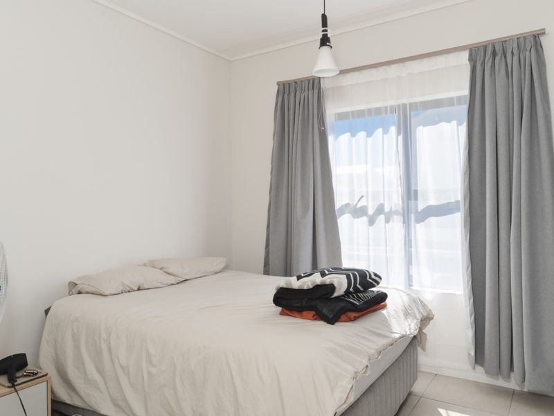A bright bedroom featuring neutral walls, tiled flooring, and a sliding window with curtains, complemented by a built-in wardrobe.