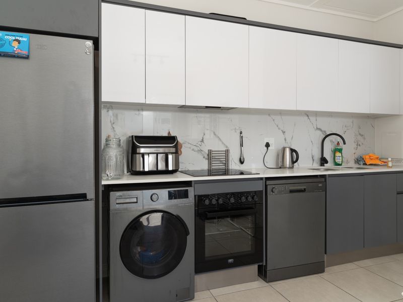 Modern kitchen featuring sleek two-tone cabinetry, marble-look splashback, integrated hob and oven, and tiled flooring with ample storage space.