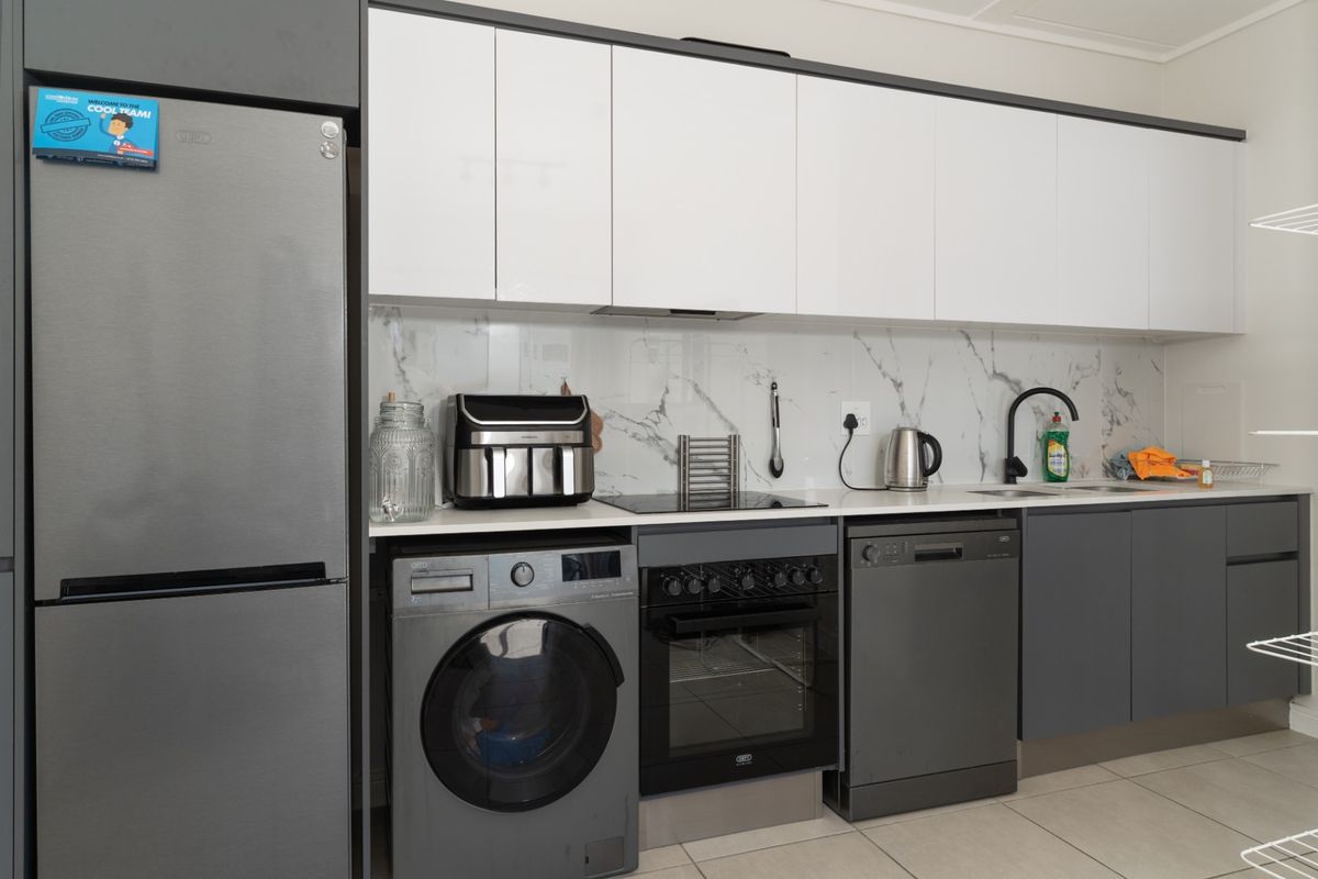 Modern kitchen featuring sleek two-tone cabinetry, marble-look splashback, integrated hob and oven, and tiled flooring with ample storage space.