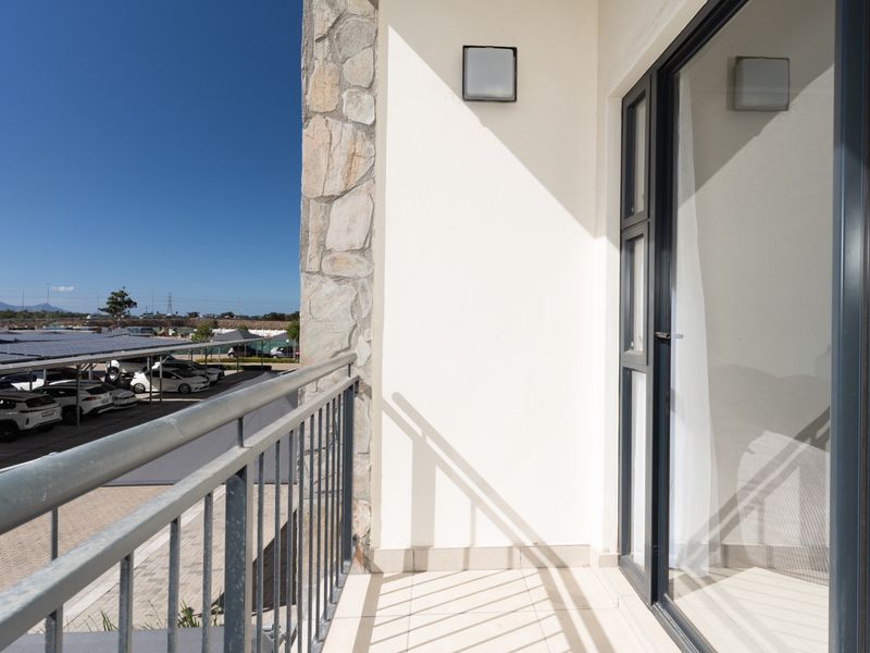 A clean, modern balcony featuring tiled flooring, a metal balustrade, and stone cladding accents, offering an open view of the parking area.
