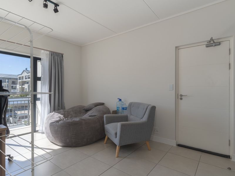 A bright living area featuring neutral tiled flooring, track lighting, and a sliding glass door providing access to a balcony.