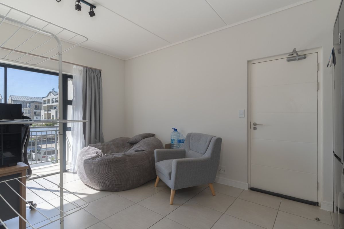 A bright living area featuring neutral tiled flooring, track lighting, and a sliding glass door providing access to a balcony.