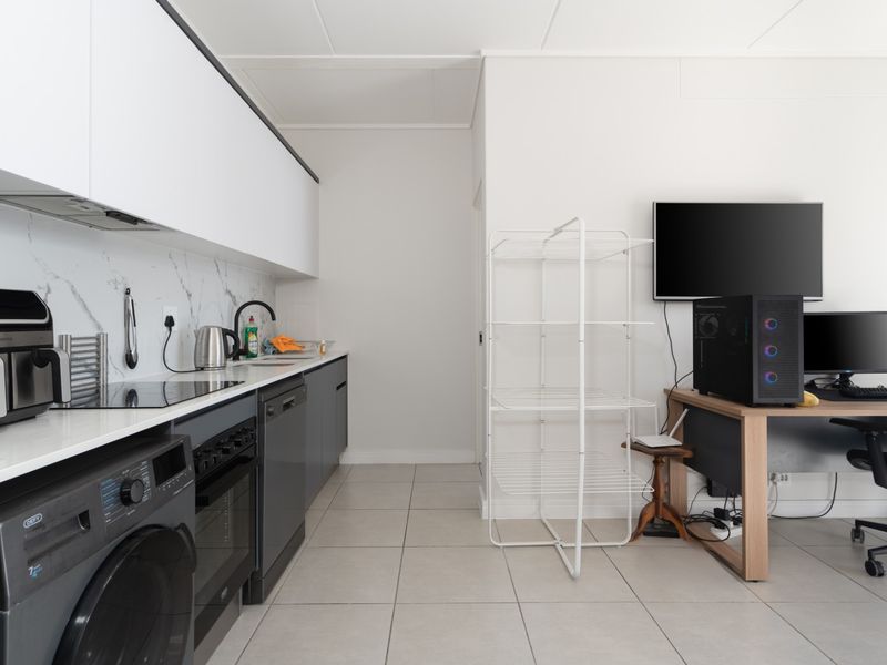 Modern open-plan kitchen featuring sleek cabinetry, marble-look splashback, and integrated appliances, seamlessly flowing into a versatile living or workspace area.