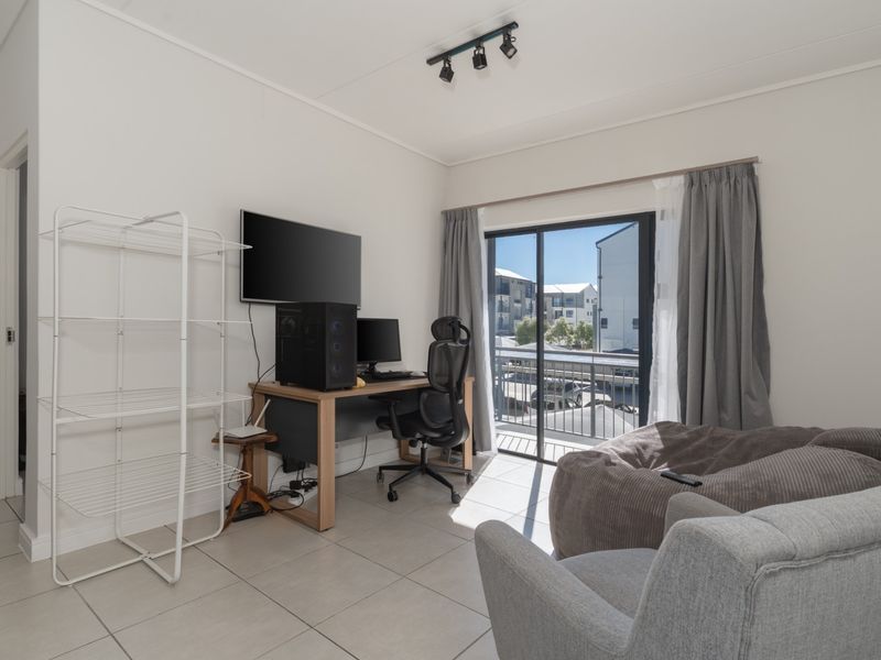 A bright living area featuring tiled flooring, track lighting, and a sliding glass door providing access to a balcony.