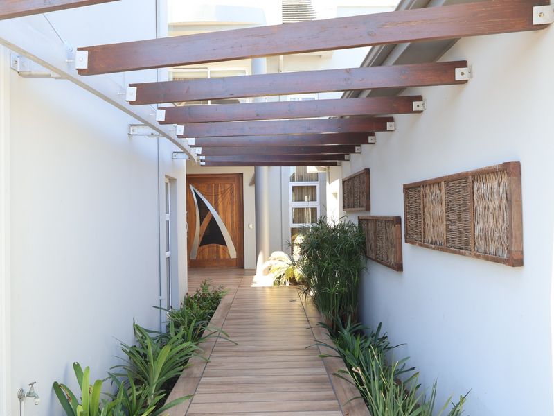 A welcoming entrance walkway featuring timber decking and a modern timber pergola leading to a decorative front door.