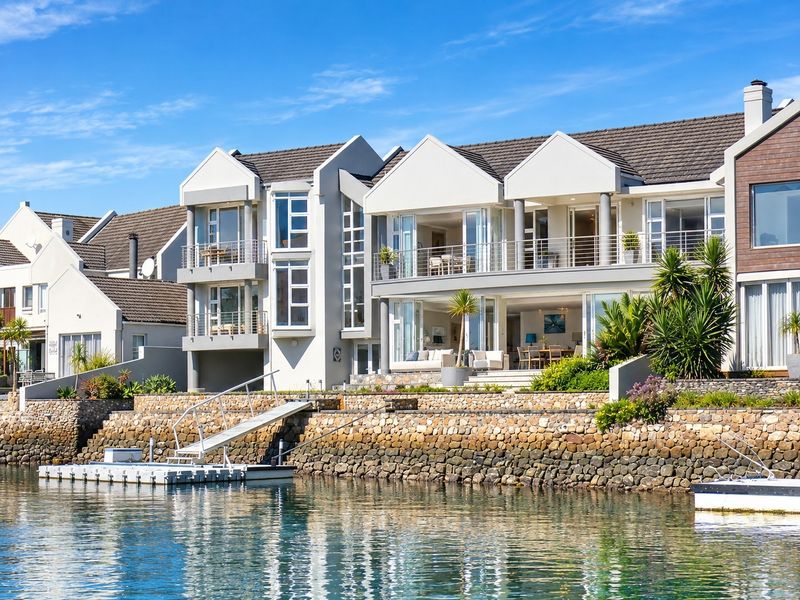 A stunning waterfront property featuring multi-level balconies, a private jetty, and direct water access, showcasing modern architectural design and well-maintained exterior finishes.