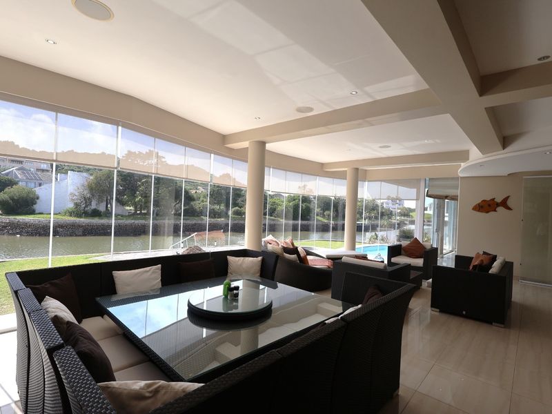 Spacious enclosed patio featuring floor-to-ceiling glass walls, tiled flooring, and recessed lighting, offering scenic views of the adjacent waterway and pool area.