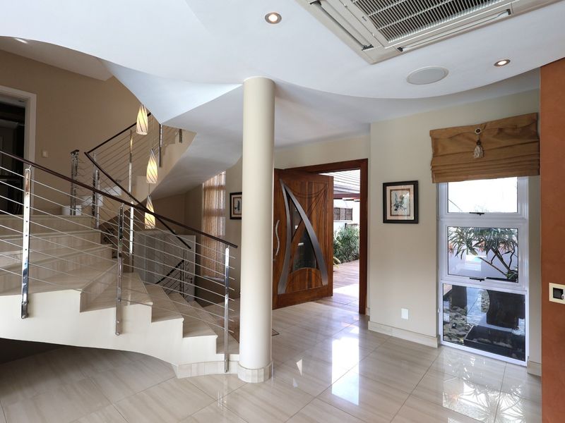 Spacious entrance hall featuring a striking curved staircase with stainless steel balustrades, polished tiled flooring, and modern recessed lighting.