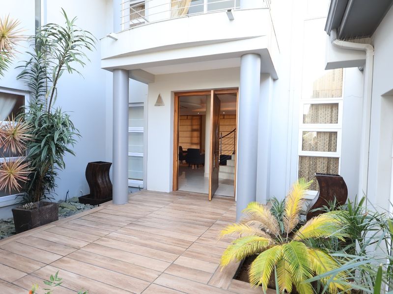 A modern entrance area featuring a tiled patio, double door access, and structural columns leading into the home.