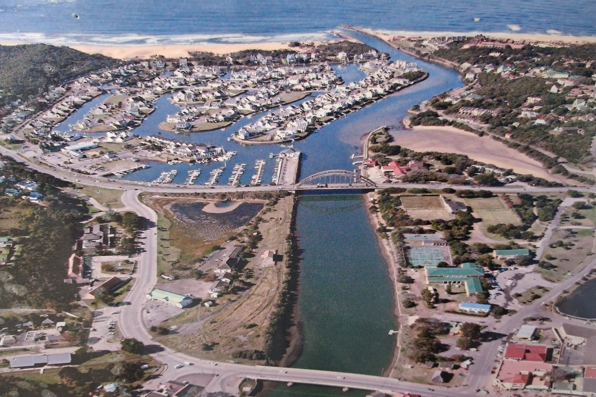 An aerial view of a coastal residential estate featuring a marina, river, and bridge infrastructure.
