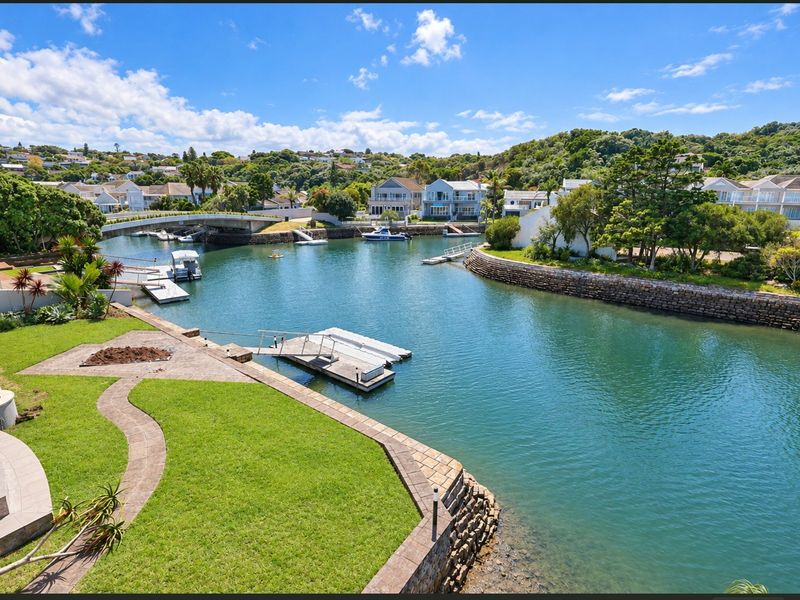 Scenic elevated view overlooking a private canal, featuring a manicured lawn, stone retaining walls, and private jetty access.
