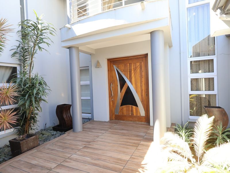 A modern entrance featuring a decorative wooden front door, tiled porch area, and structural columns leading into the home.
