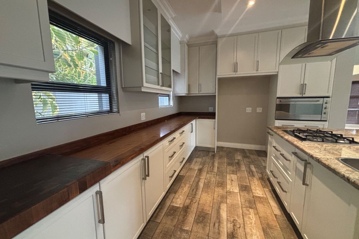 Modern kitchen featuring white cabinetry, wooden and granite countertops, built-in gas hob, oven, and extractor fan with wood-look tiled flooring.