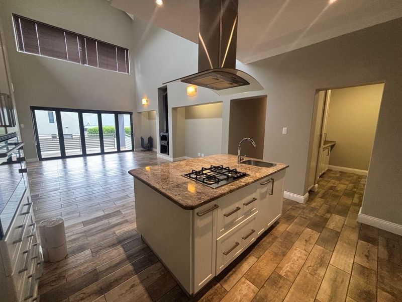 Spacious open-plan living area featuring a modern kitchen island with gas hob, granite countertops, and seamless flow to the outdoor patio through bi-fold doors.