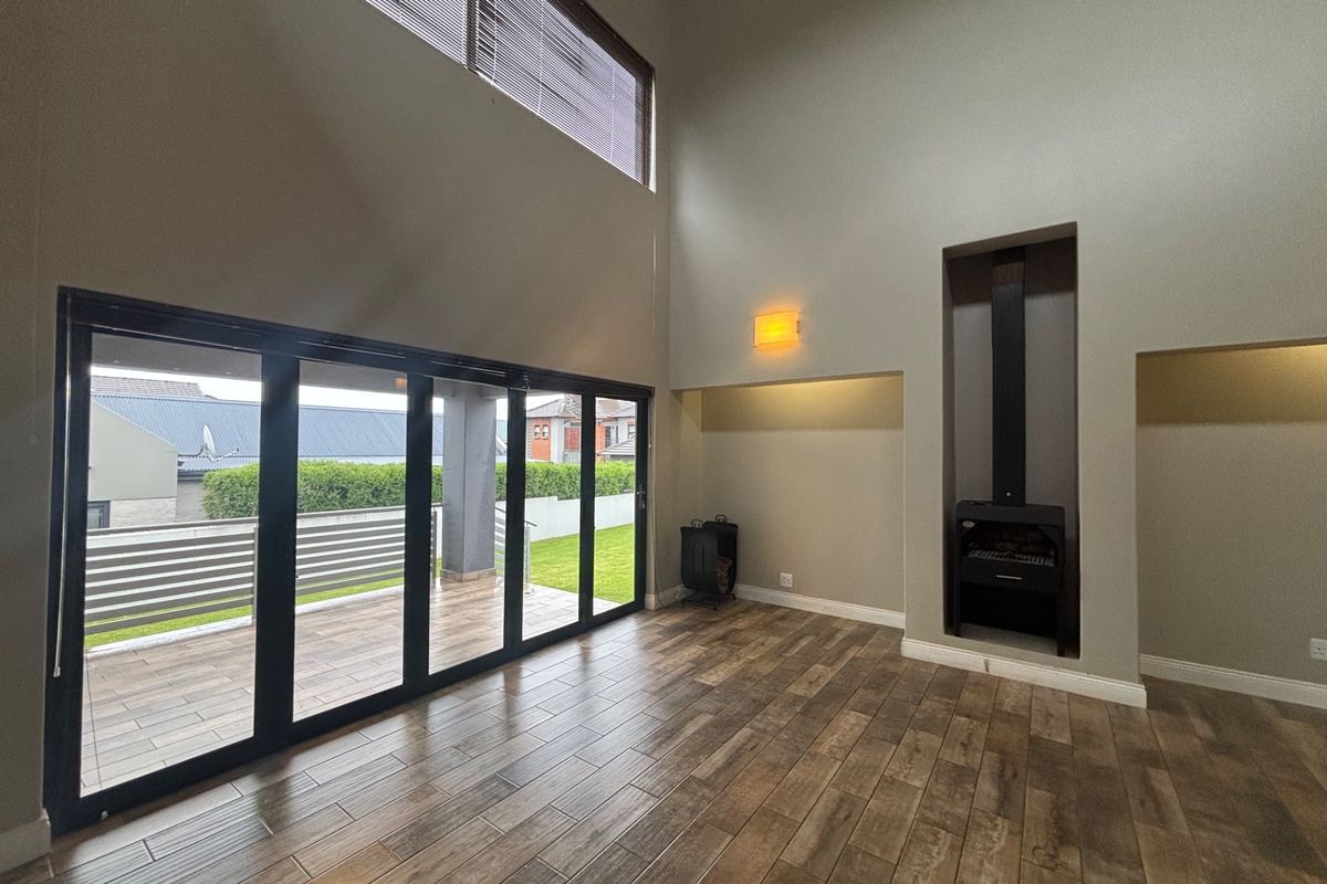 Spacious double-volume living area featuring wood-look tiled flooring, a built-in fireplace, and large stacking doors opening onto an outdoor patio.