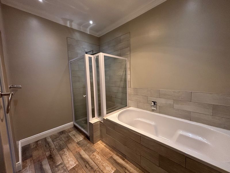 Modern bathroom featuring a built-in bathtub, separate glass shower enclosure, and contemporary wood-look tile flooring with neutral wall finishes.