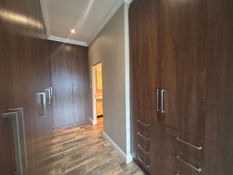 A spacious dressing area featuring extensive built-in wooden cabinetry, tiled flooring, and recessed lighting, leading directly into an adjoining bathroom.