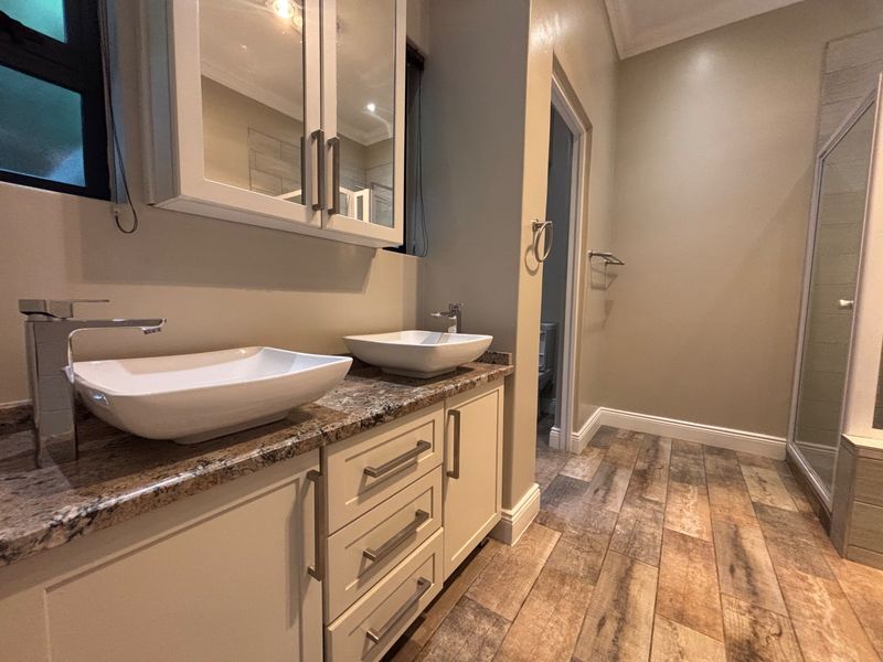 Modern bathroom featuring a double vanity with granite countertops, vessel sinks, wood-look tile flooring, and a separate walk-in shower.