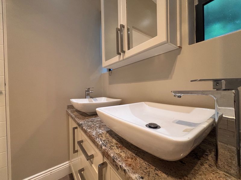 Modern bathroom vanity featuring a granite countertop, dual vessel sinks with chrome faucets, and a wall-mounted mirrored medicine cabinet.