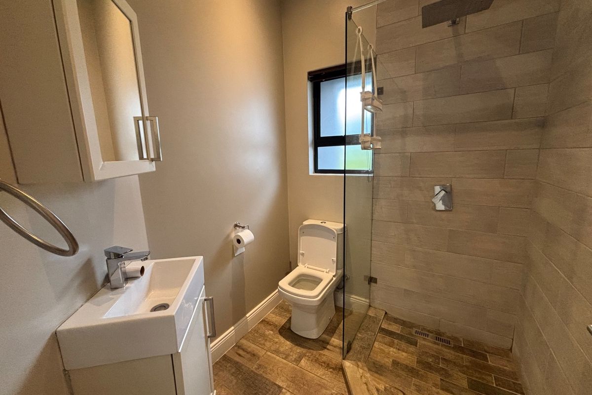 Modern bathroom featuring a walk-in shower with glass screen, rain shower head, vanity cabinet with basin, and wood-look floor tiles.