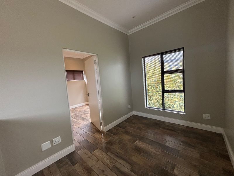 An empty bedroom featuring wood-look tile flooring, neutral walls, cornice detailing, and an aluminium window with fitted blinds.