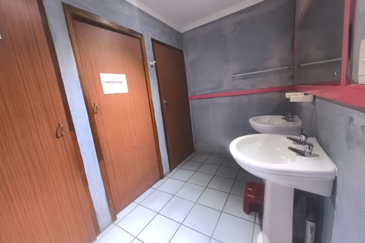 A functional commercial bathroom featuring dual pedestal wash basins, tiled flooring, and multiple wooden doors.