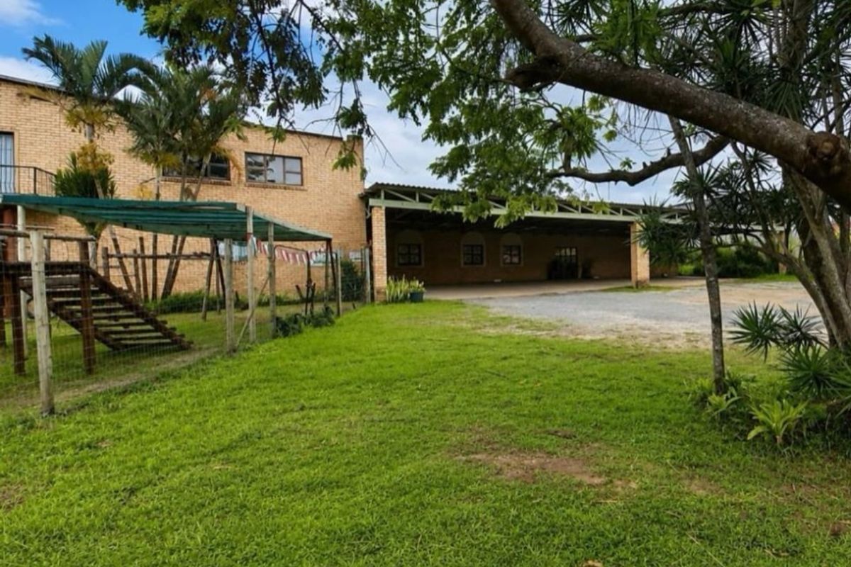 Rear view of a commercial property featuring a face brick facade, a large covered patio area, and an expansive lawn.