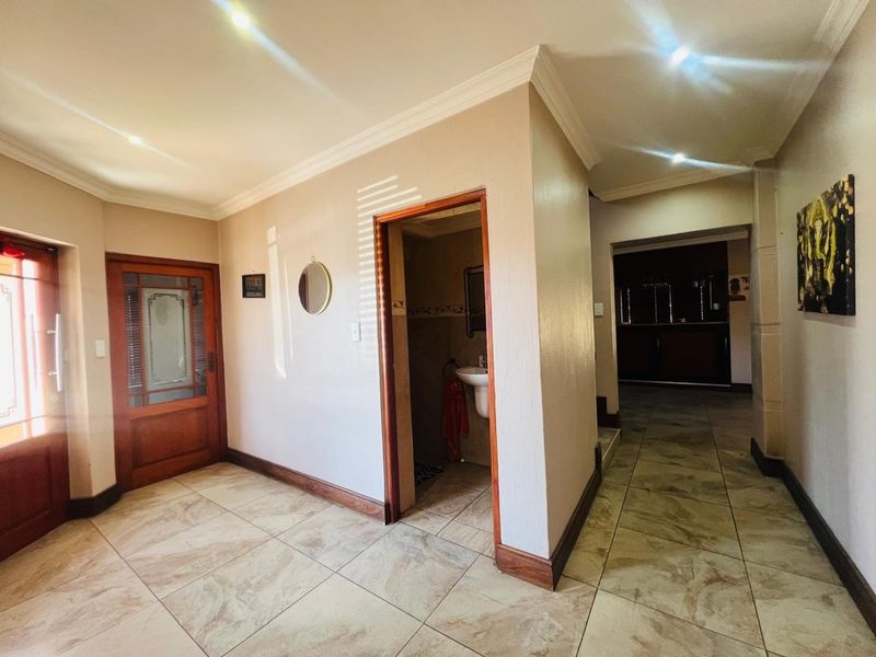 A spacious tiled hallway featuring recessed lighting, decorative cornicing, and access to a guest bathroom with a pedestal basin.