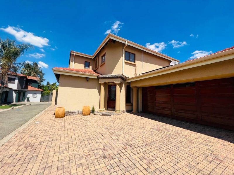 Front elevation of a double-story house featuring a paved driveway, integrated double garage, and a covered entrance with decorative pillars.