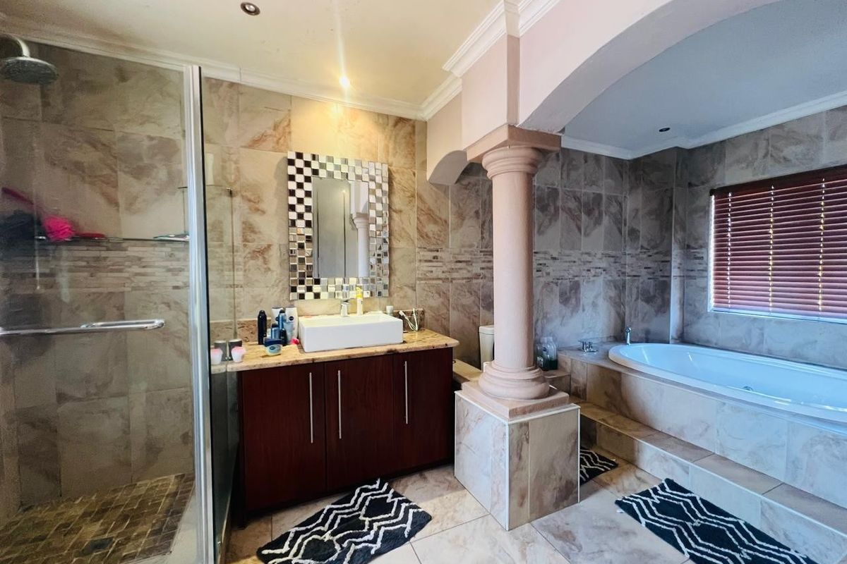 Spacious bathroom featuring a glass shower enclosure, built-in vanity with vessel sink, and a sunken bathtub with tiled surround and decorative column.