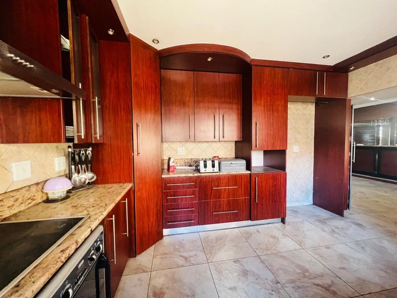 A functional kitchen featuring rich wood-toned cabinetry, granite countertops, a built-in hob, and tiled flooring with a neutral backsplash.