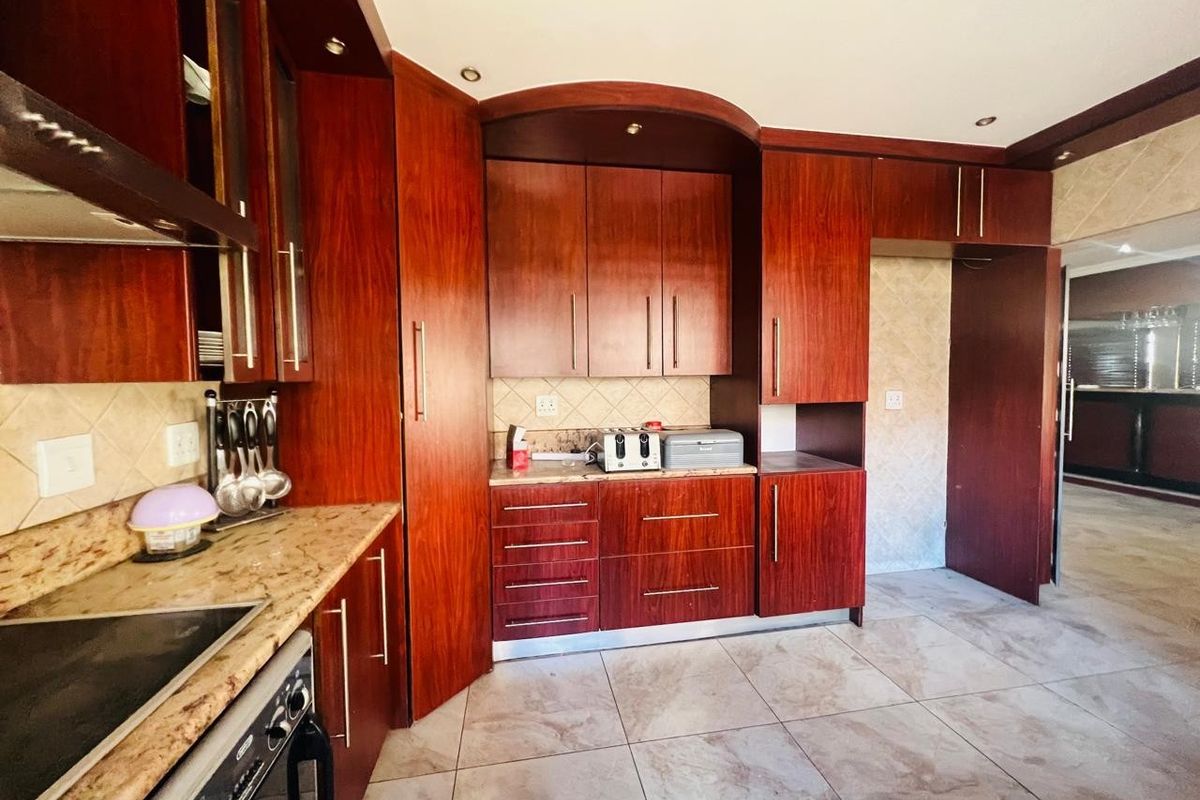 A functional kitchen featuring rich wood-toned cabinetry, granite countertops, a built-in hob, and tiled flooring with a neutral backsplash.