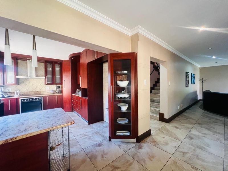 Open-plan kitchen and living area featuring dark wood cabinetry, stone-look tile flooring, and a central kitchen island, with an adjacent staircase.