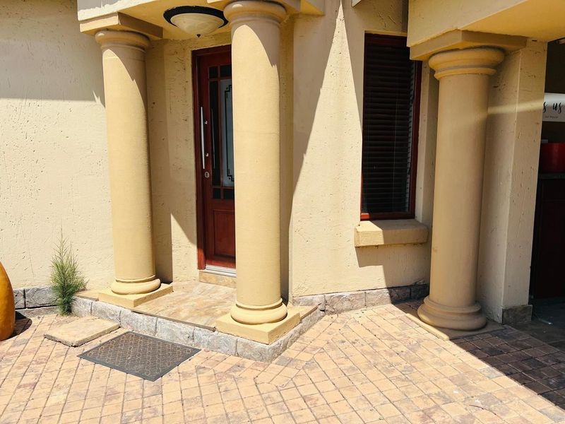 A welcoming entrance featuring classical columns, a timber front door, and a paved porch area.
