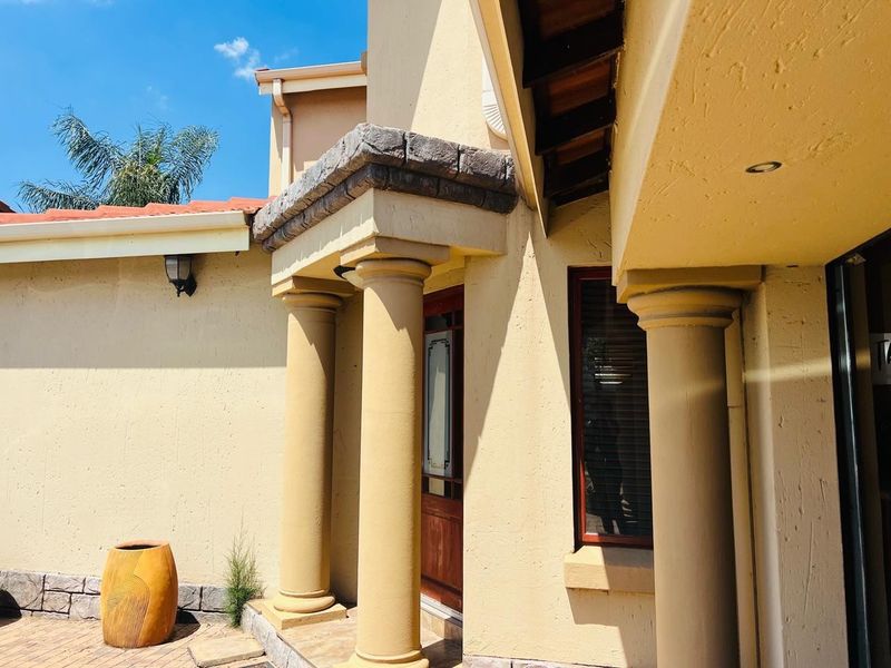 Front entrance area featuring classical columns, a stone-clad lintel, and a timber door, set against a paved driveway and rendered exterior walls.