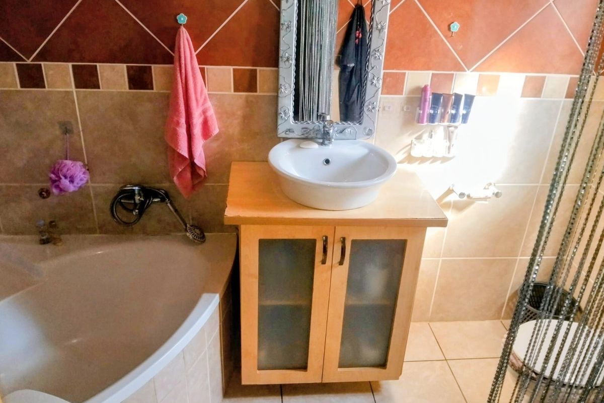 A bathroom featuring a corner bathtub, a vessel sink set on a wooden vanity cabinet, and decorative tiled walls.