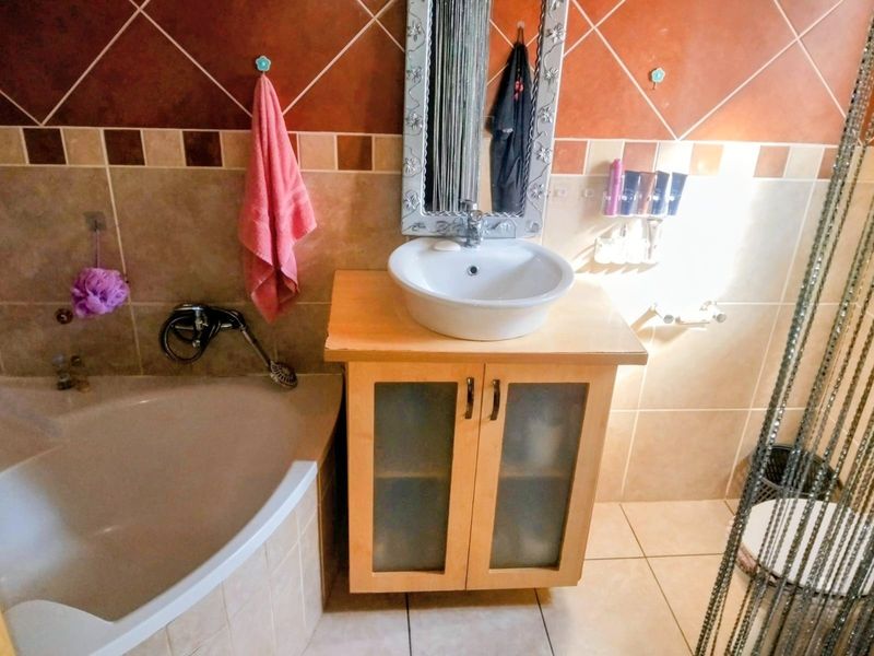A bathroom featuring a corner bathtub, a vessel sink set on a wooden vanity cabinet, and decorative tiled walls.