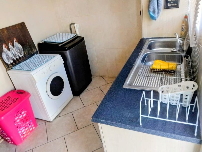 Functional laundry area featuring a double stainless steel sink, laminate countertop, and tiled splashback with practical floor tiling.