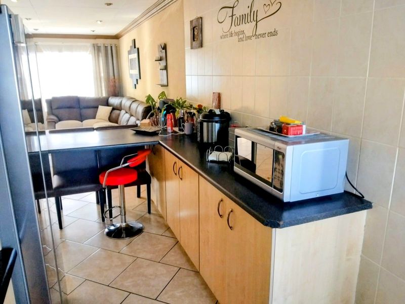 Open-plan kitchen and living area featuring laminate cabinetry, a breakfast bar, and neutral ceramic tiling throughout.