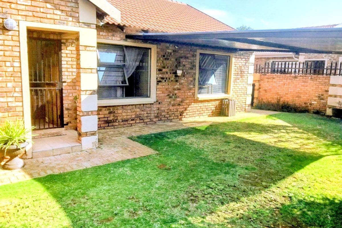 Rear view of a face brick townhouse featuring a paved patio area, attached carport, and a private garden space.