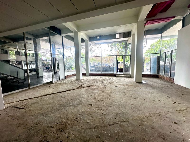 Spacious open-plan commercial area featuring extensive floor-to-ceiling glass windows, exposed structural columns, and unfinished concrete flooring, offering a versatile blank canvas for renovation.