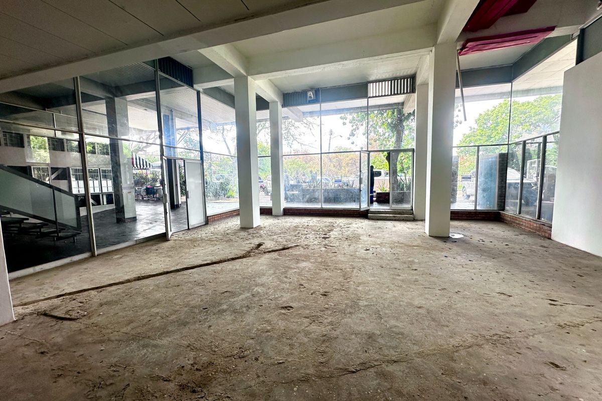 Spacious open-plan commercial area featuring extensive floor-to-ceiling glass windows, exposed structural columns, and unfinished concrete flooring, offering a versatile blank canvas for renovation.